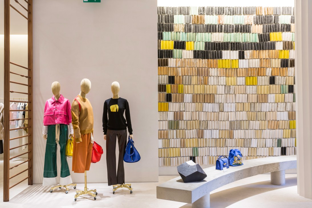 Casa Loewe flagship store interior with three mannequins displaying colorful clothing and a wall of fabric swatches.
