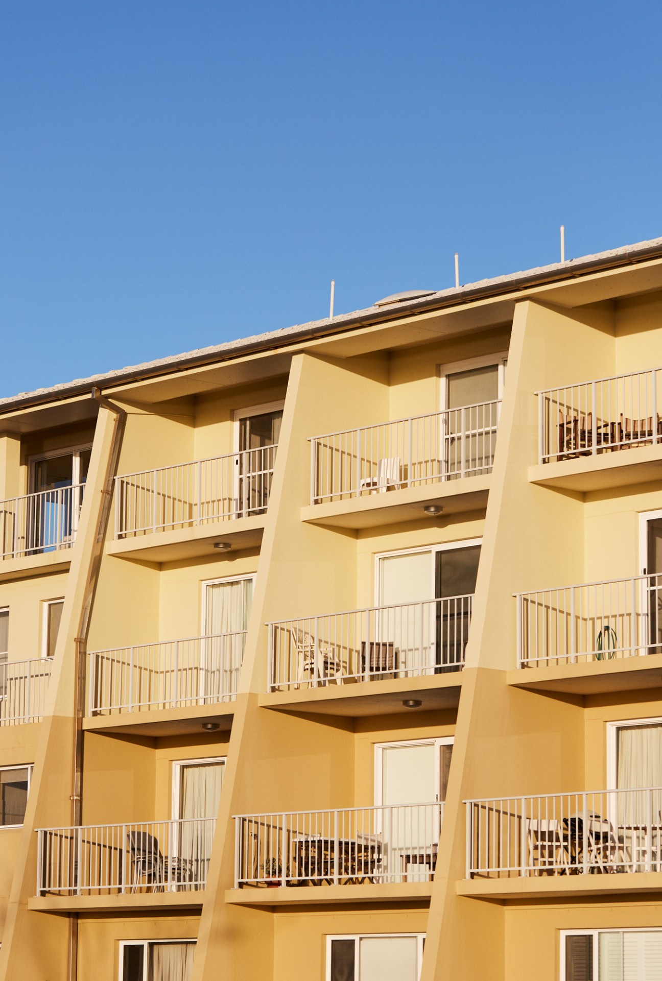 Yellow beachside apartment building with multiple balconies and white railings against clear blue sky.