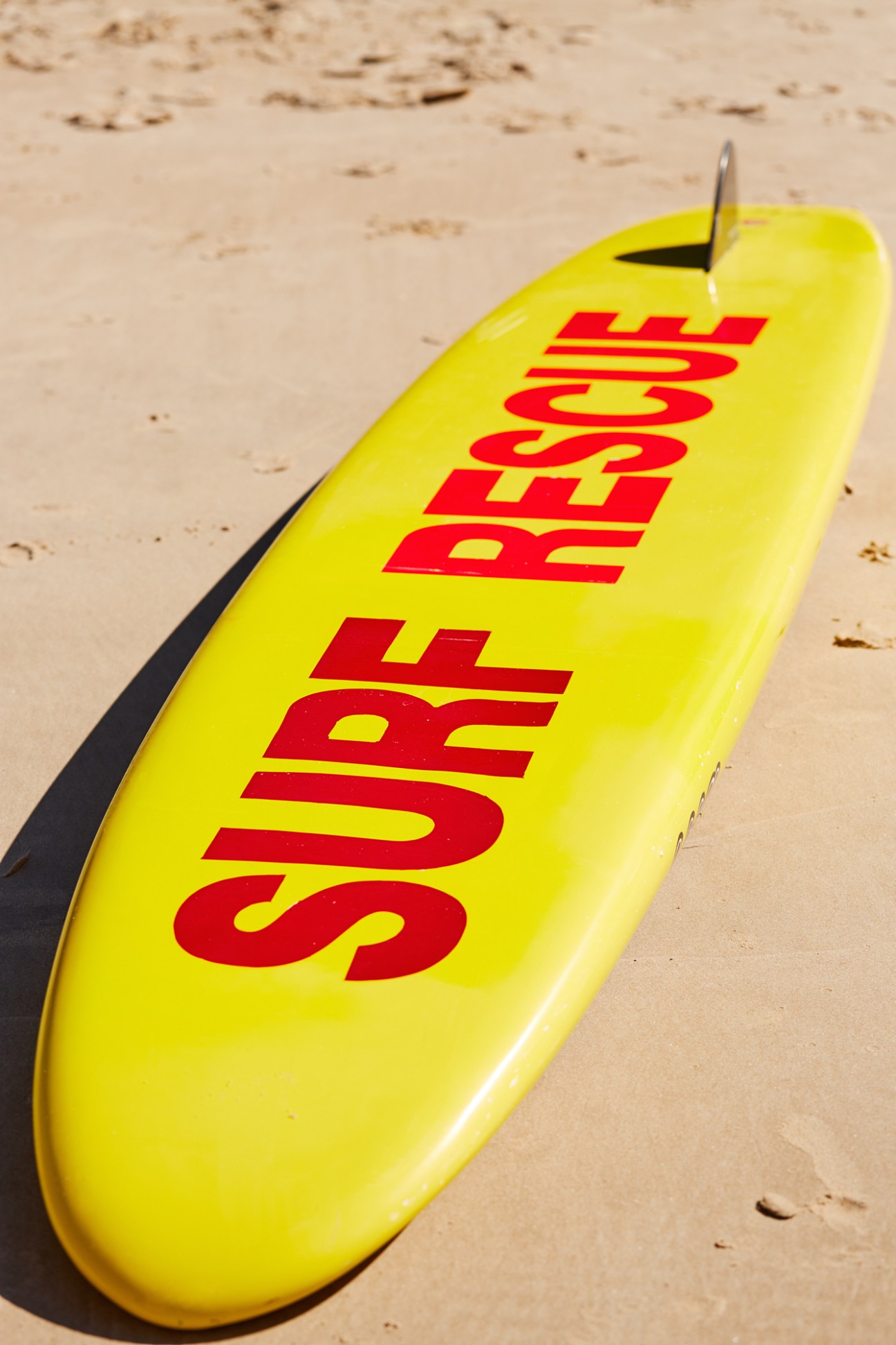 Yellow surfboard with red text reading "Surf Rescue" lying on sand at Main Beach.