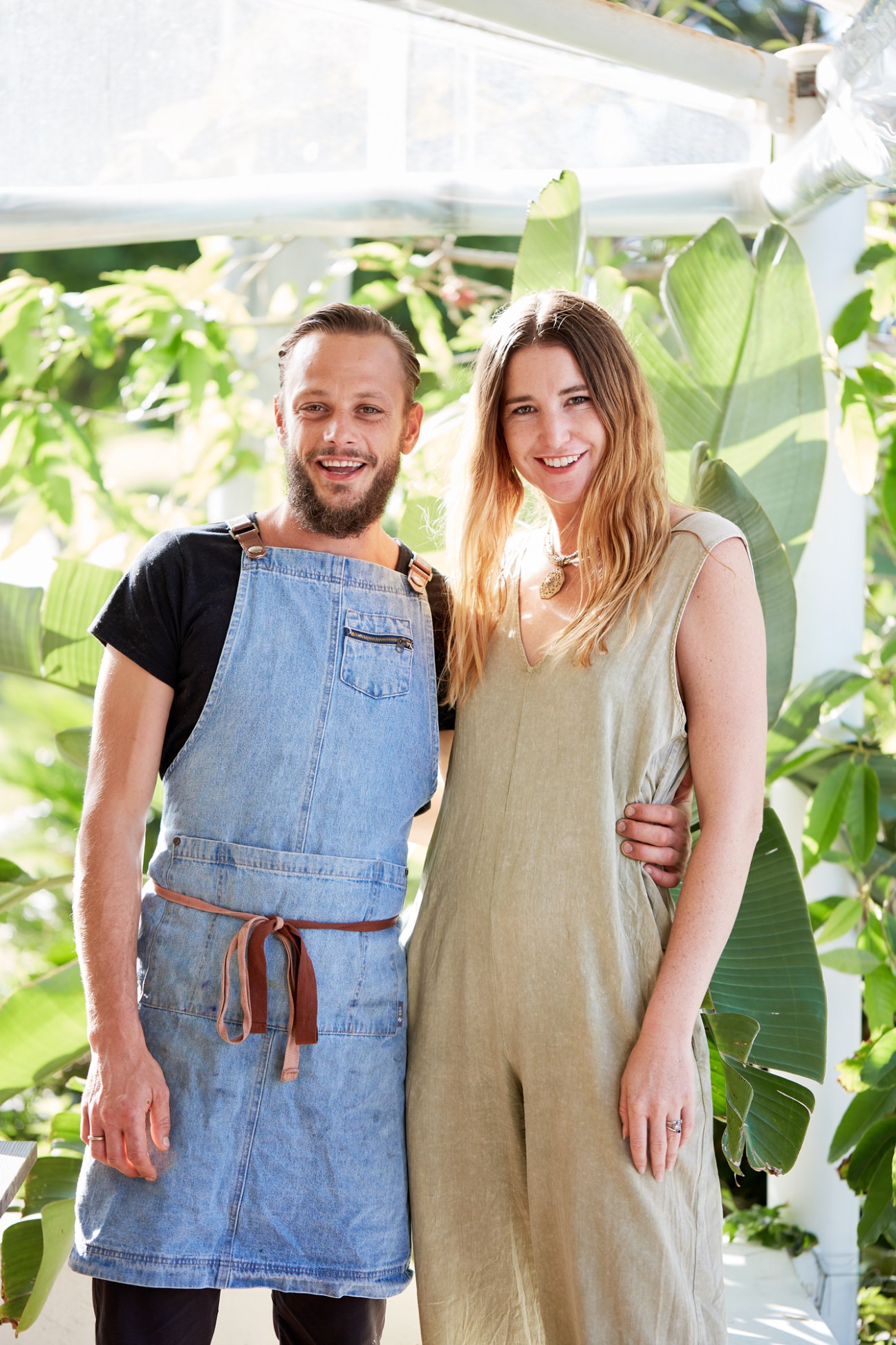 French chef Charles-Etienne Prétet and his wife Merindah Byrne Prétet standing together in a greenhouse surrounded by green foliage.