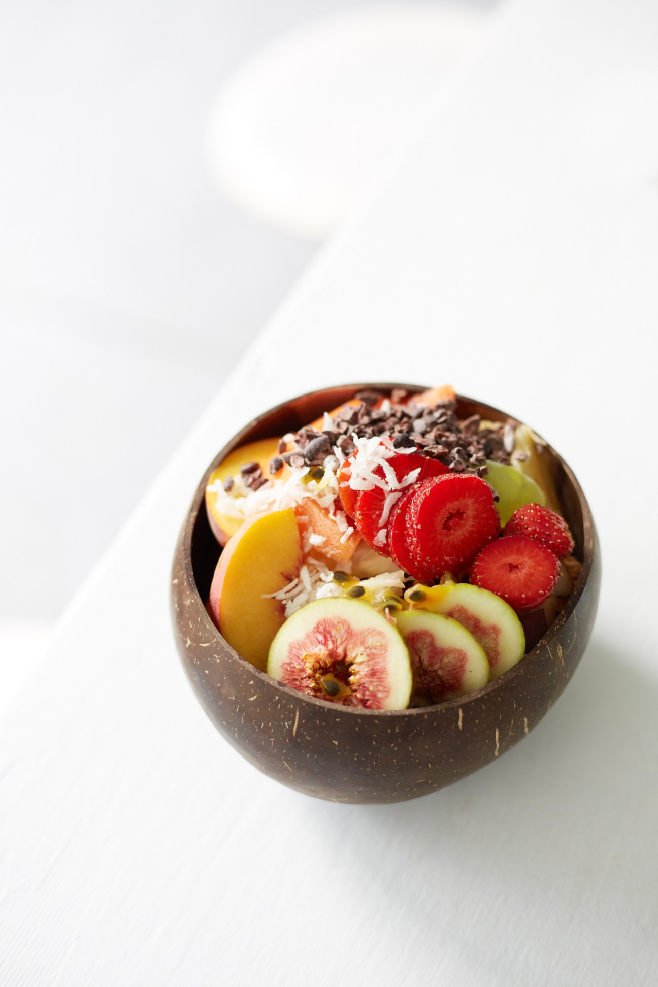 Coconut bowl filled with fresh fruit, yogurt, granola and chocolate chips including raspberries and figs.