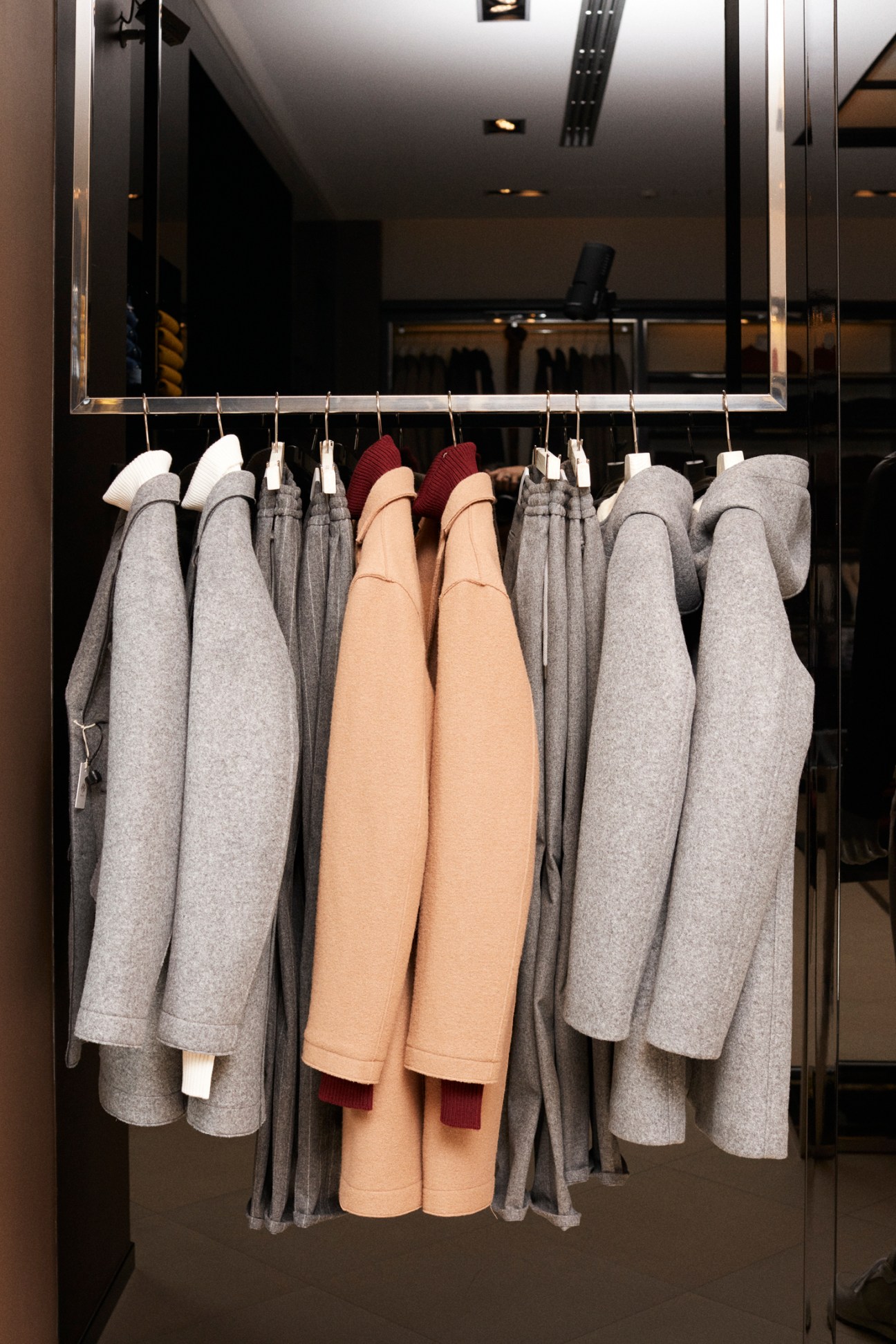Gray and beige blazers and coats hung on a rail in a modern boutique window display.