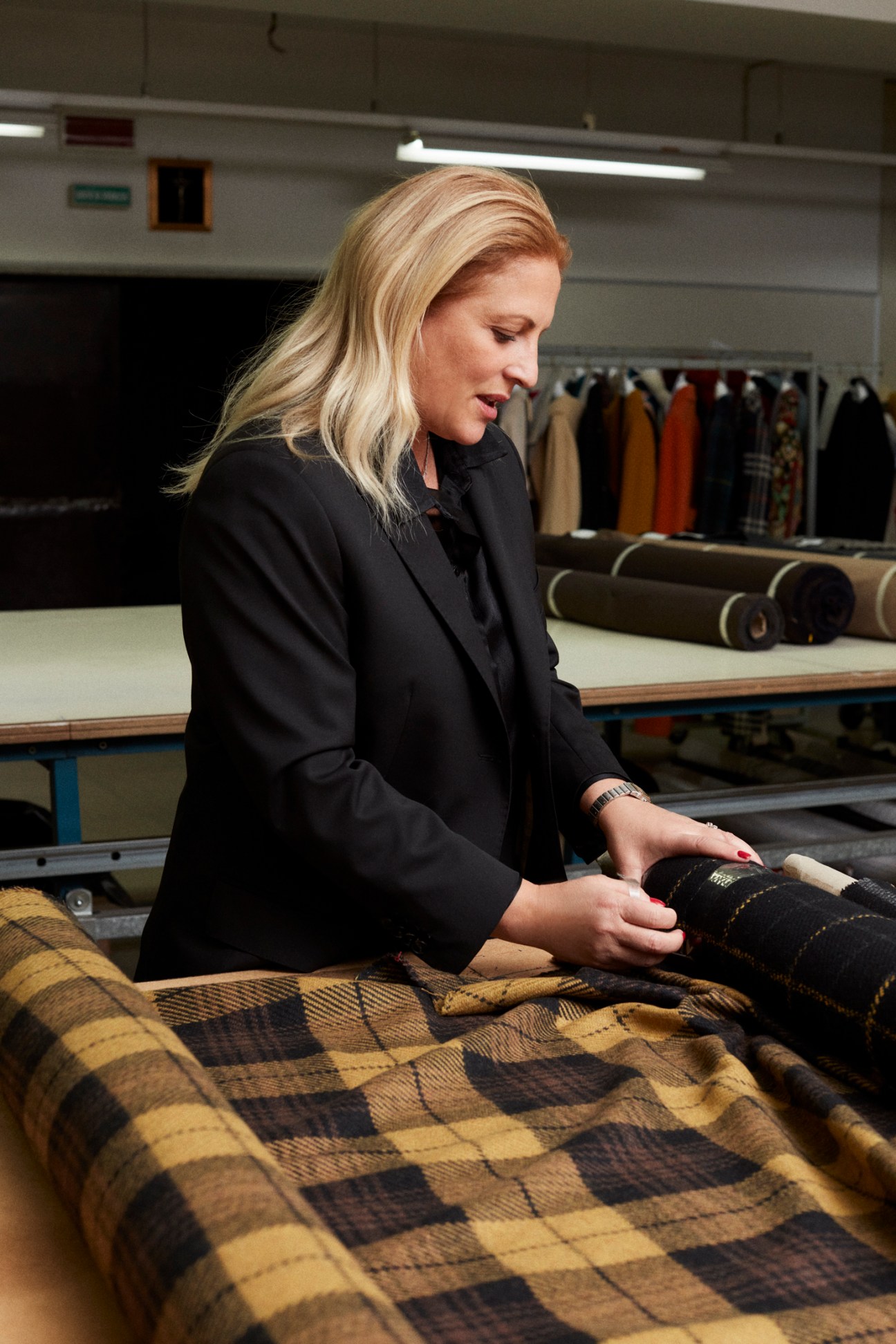 Woman in black blazer examining fabric swatches in a factory workshop.