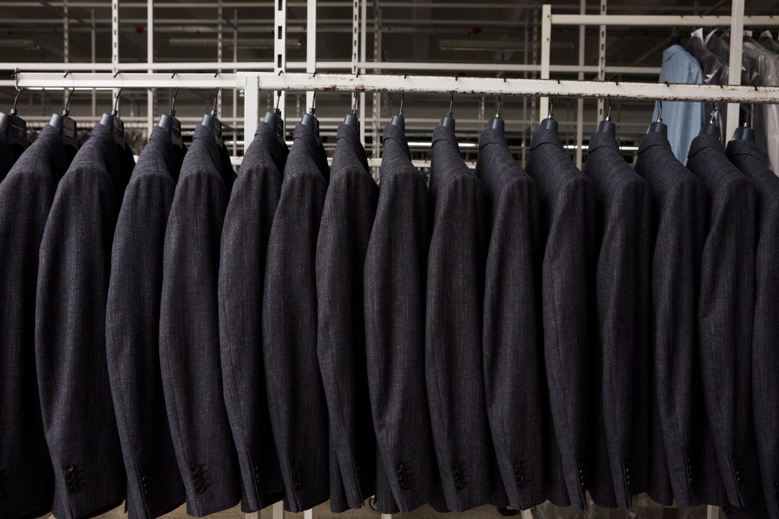 Row of dark blue blazers hanging on a metal rail ready for shipment at Eurofashion factory.