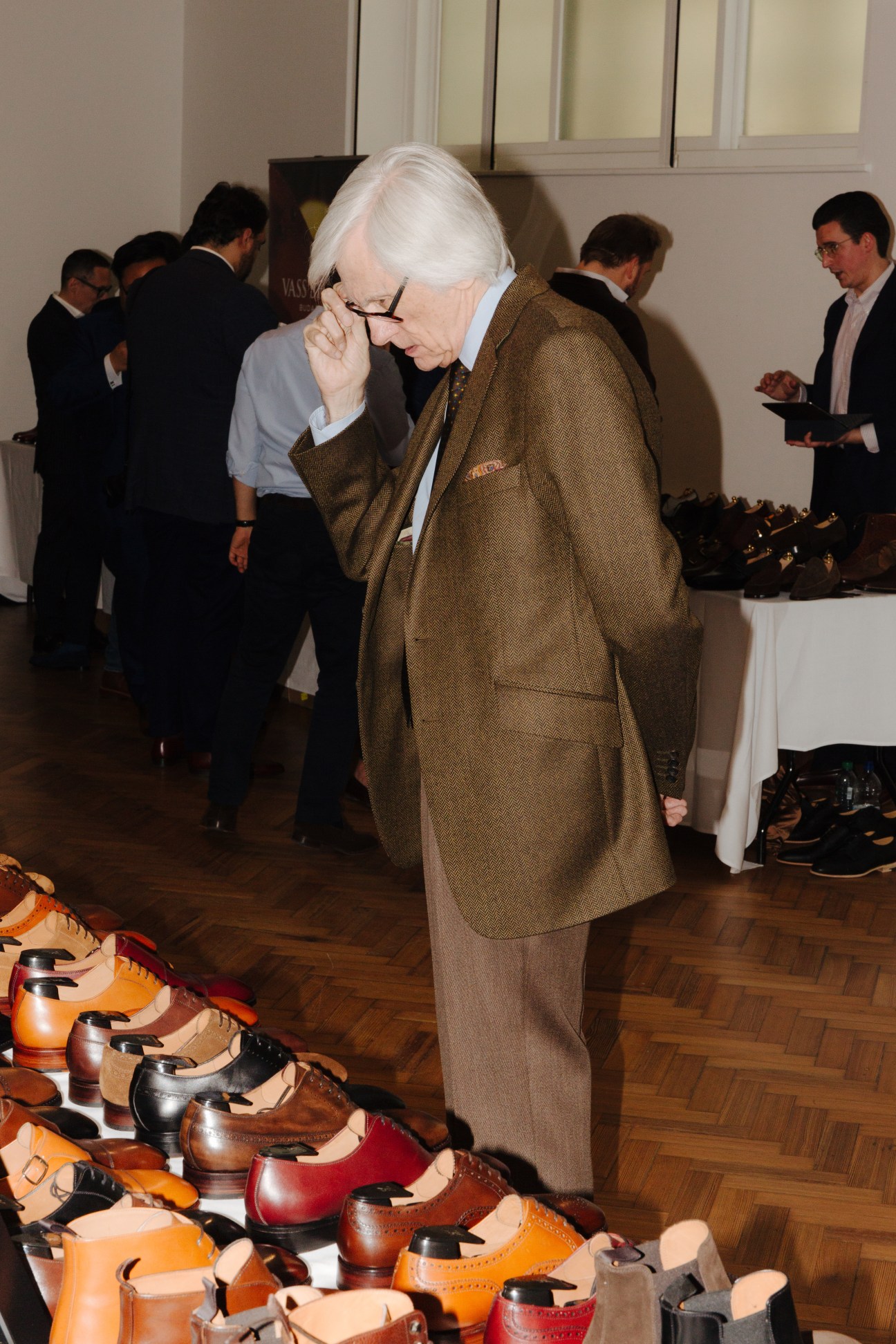 An older man with white hair in a brown blazer examines shoes on display at a shoe-shining competition.