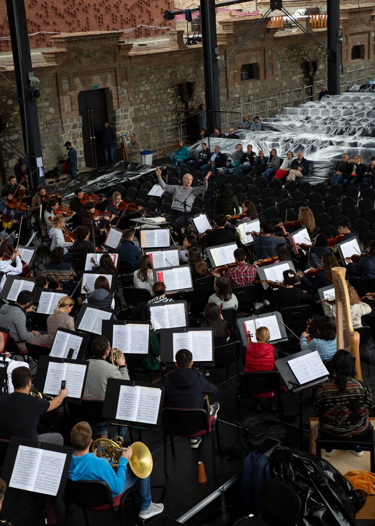 Pan-Caucasian Youth Orchestra rehearsing Mahler's second symphony in a stone hall with conductor leading ensemble.