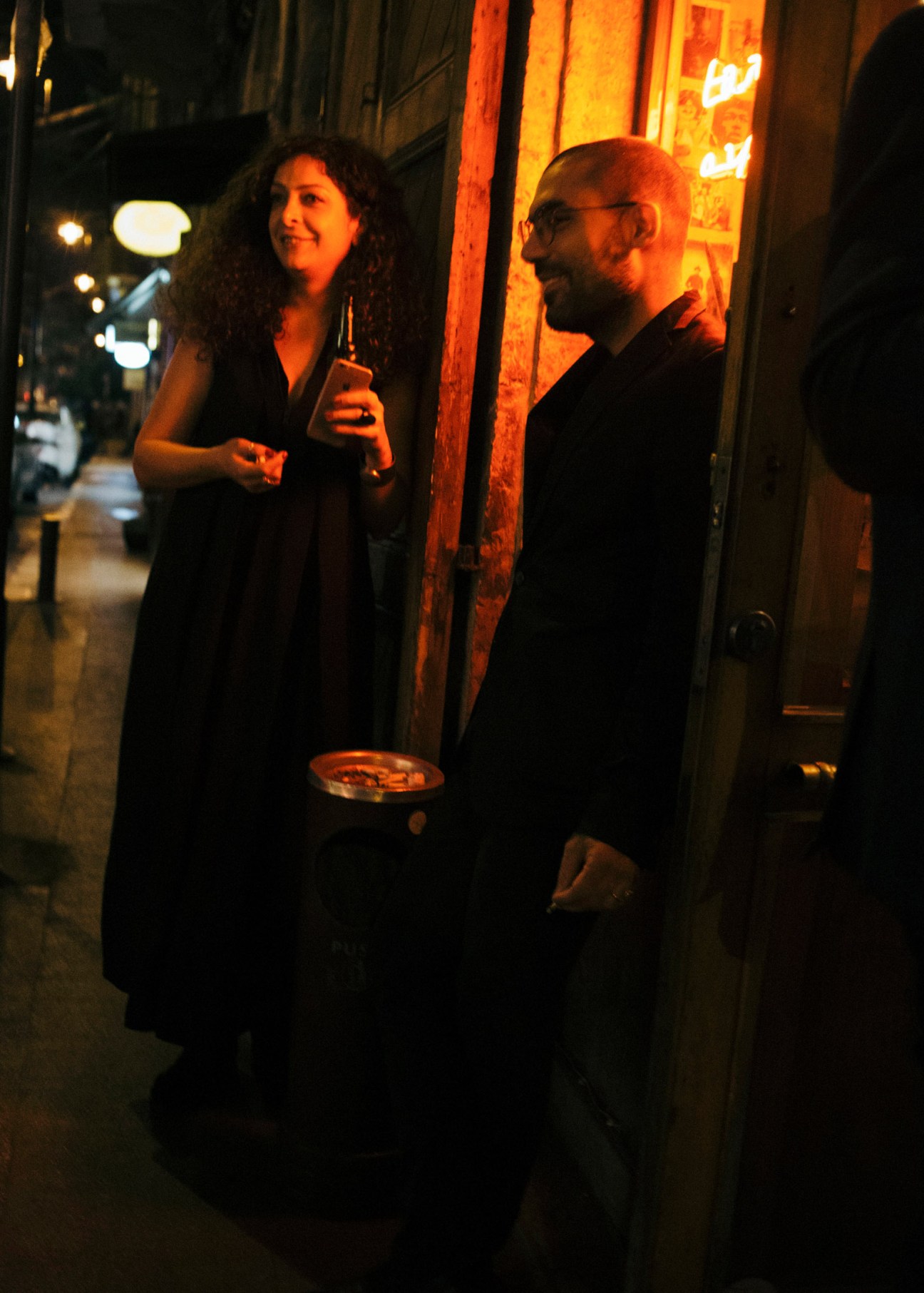 Two people hold drinks while socializing on a dimly lit Beirut street at night.