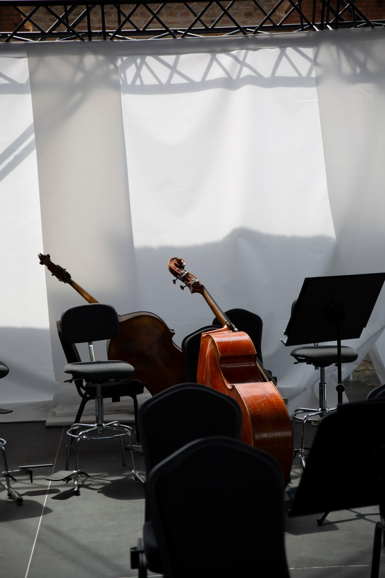 Orchestra musicians sitting with instruments during a break, with white fabric draping and steel framework visible above.