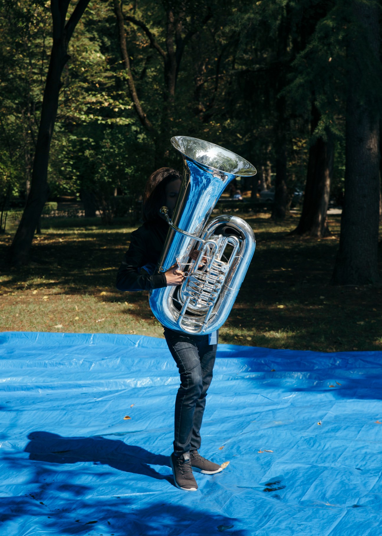 Israeli tubist Guy Cohen Hanoch holds a large tuba with blue and silver finish in a forest clearing.