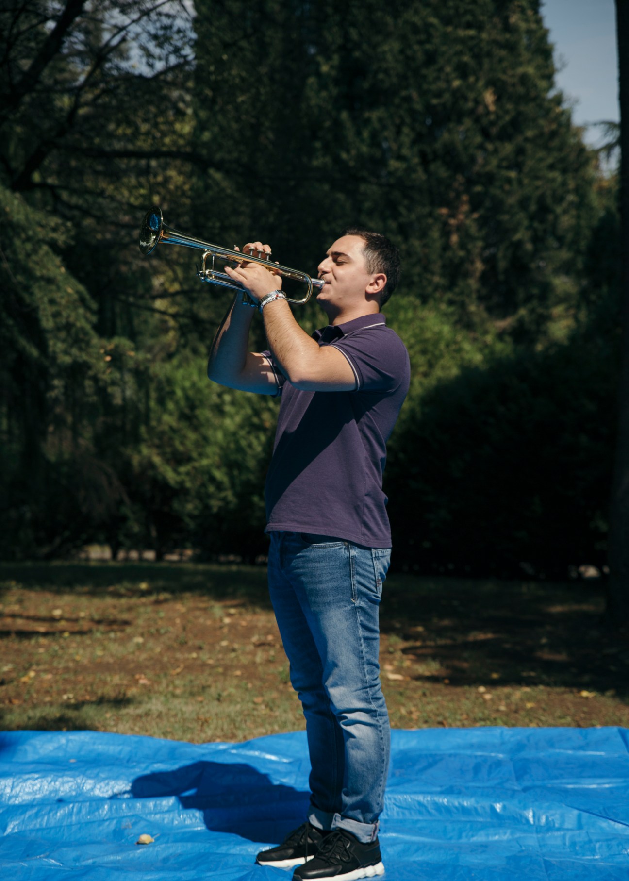 Armenian trumpeter Narek Grigoryan plays trumpet outdoors with evergreen trees in the background.