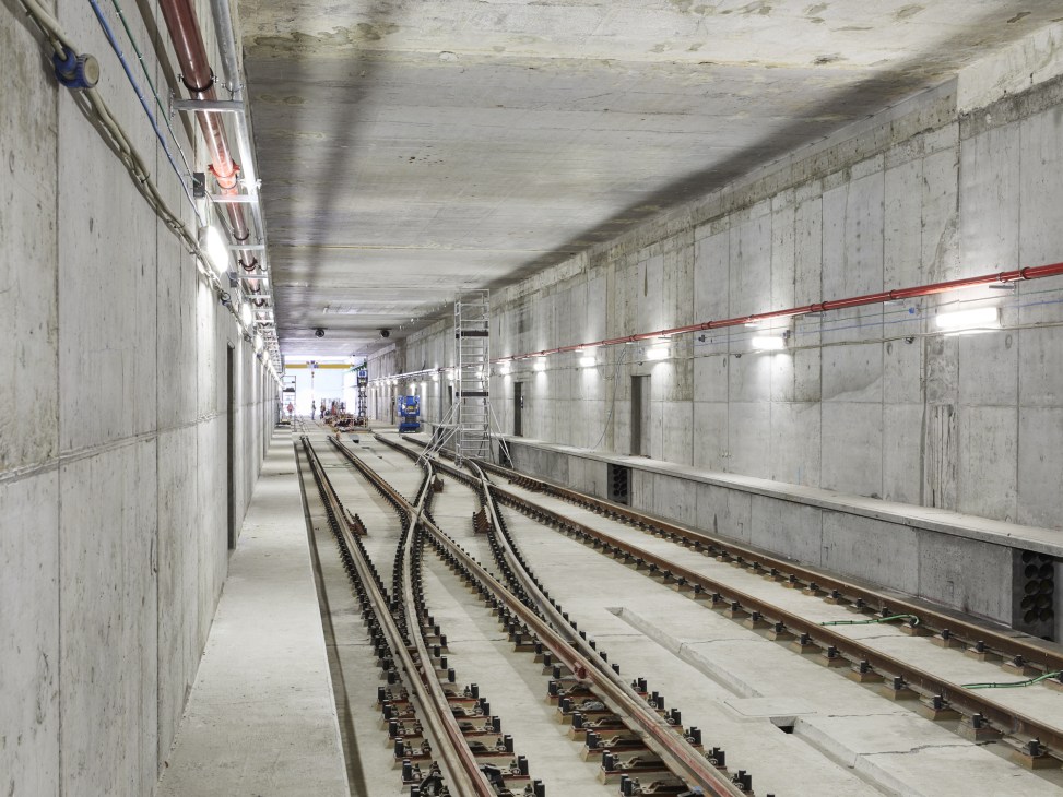 Underground metro tunnel under construction with newly laid railway tracks and concrete walls.