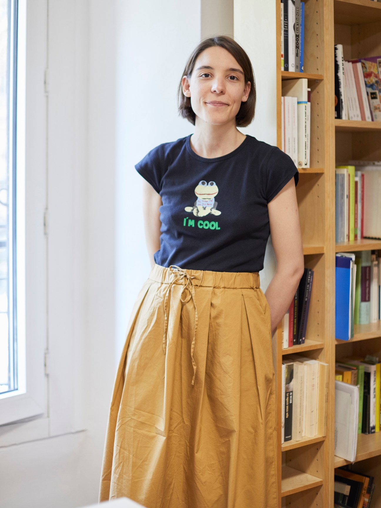 Beatrice Martelli standing in front of bookshelves wearing a dark t-shirt and mustard yellow skirt