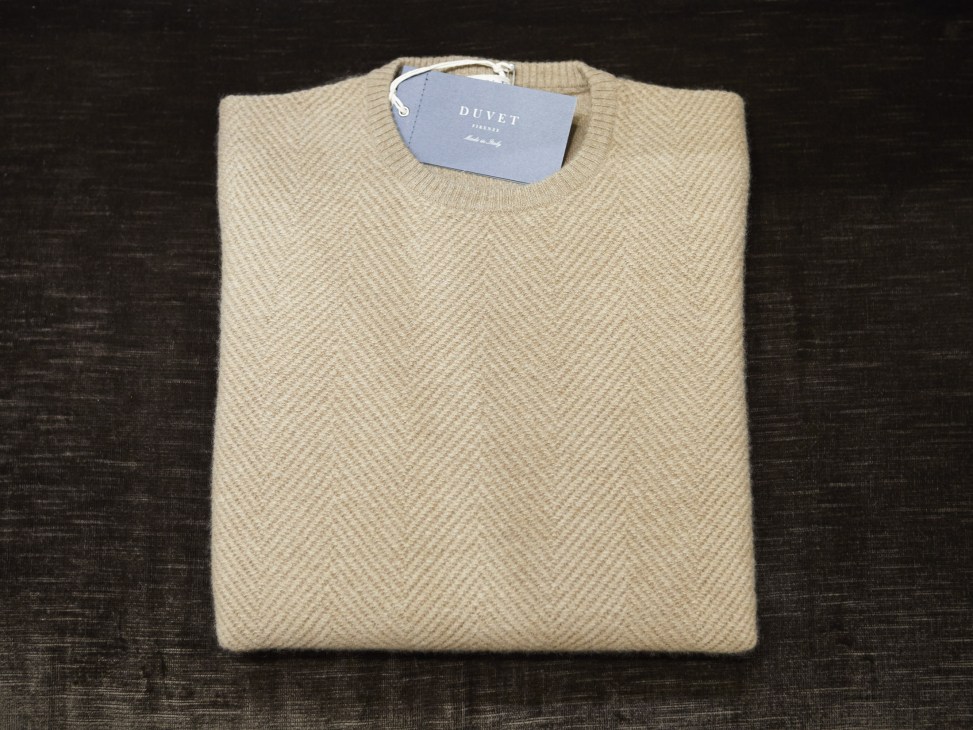 Cream-colored knit sweater with Duvet brand tag folded on dark surface