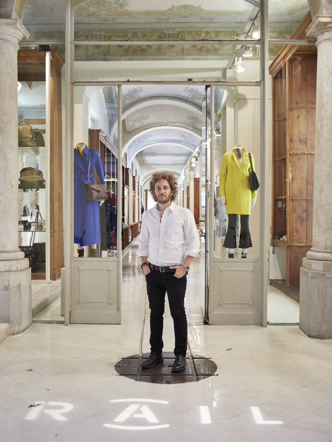 Man standing in Rail boutique interior with colourful dressed mannequins in display windows
