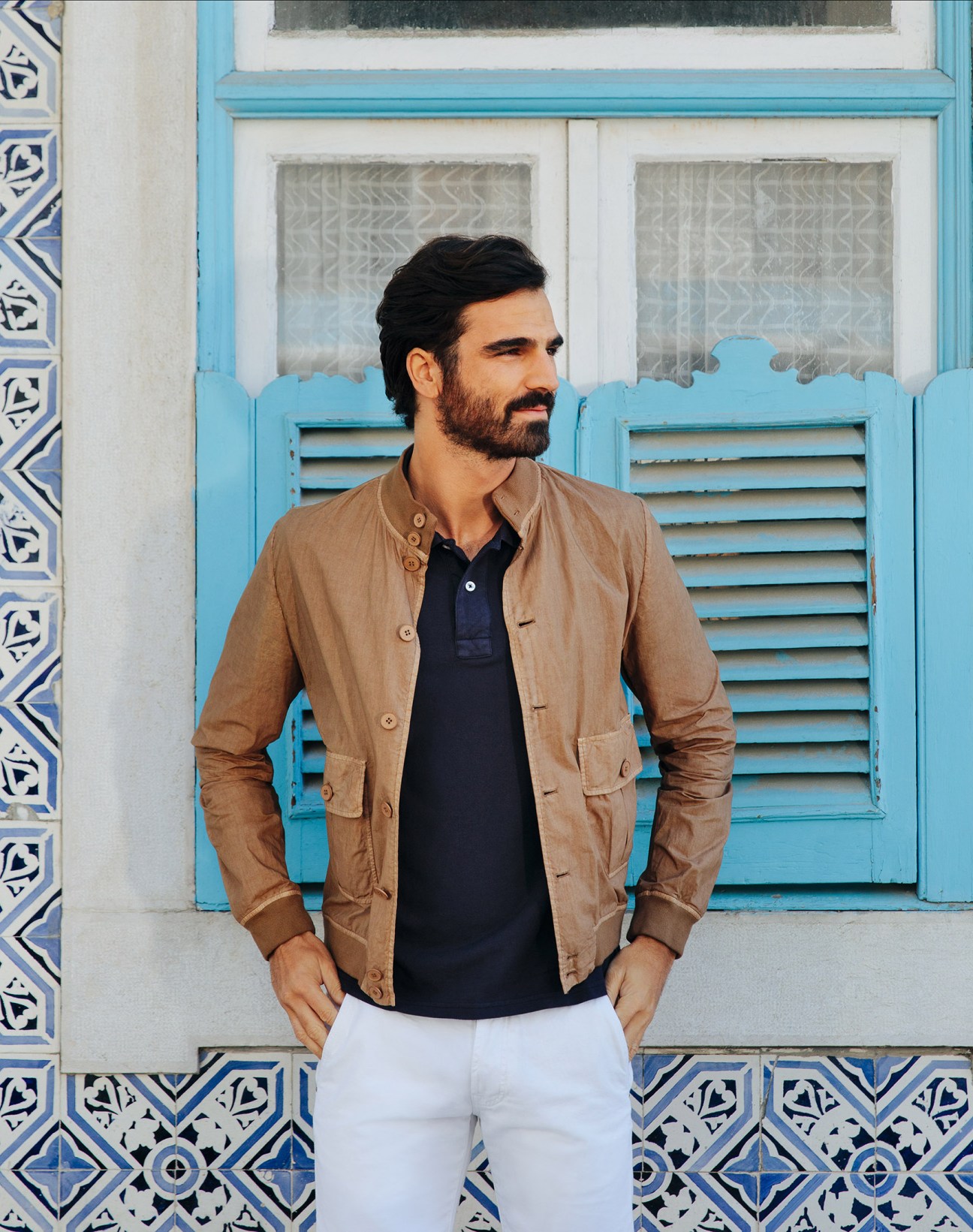 Man wearing a beige Valstar jacket and navy Parajumpers polo shirt against a blue and white tiled Lisbon building.