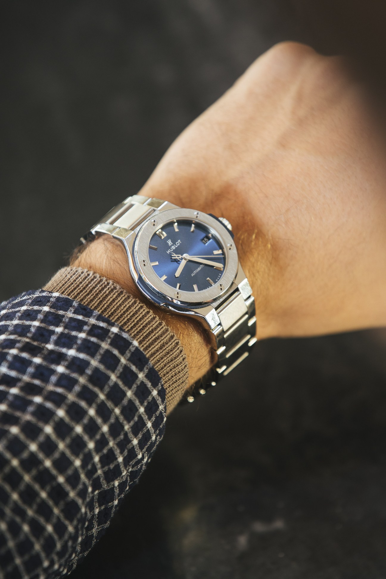 Hublot watch with blue dial on wrist wearing patterned navy and tan sweater.