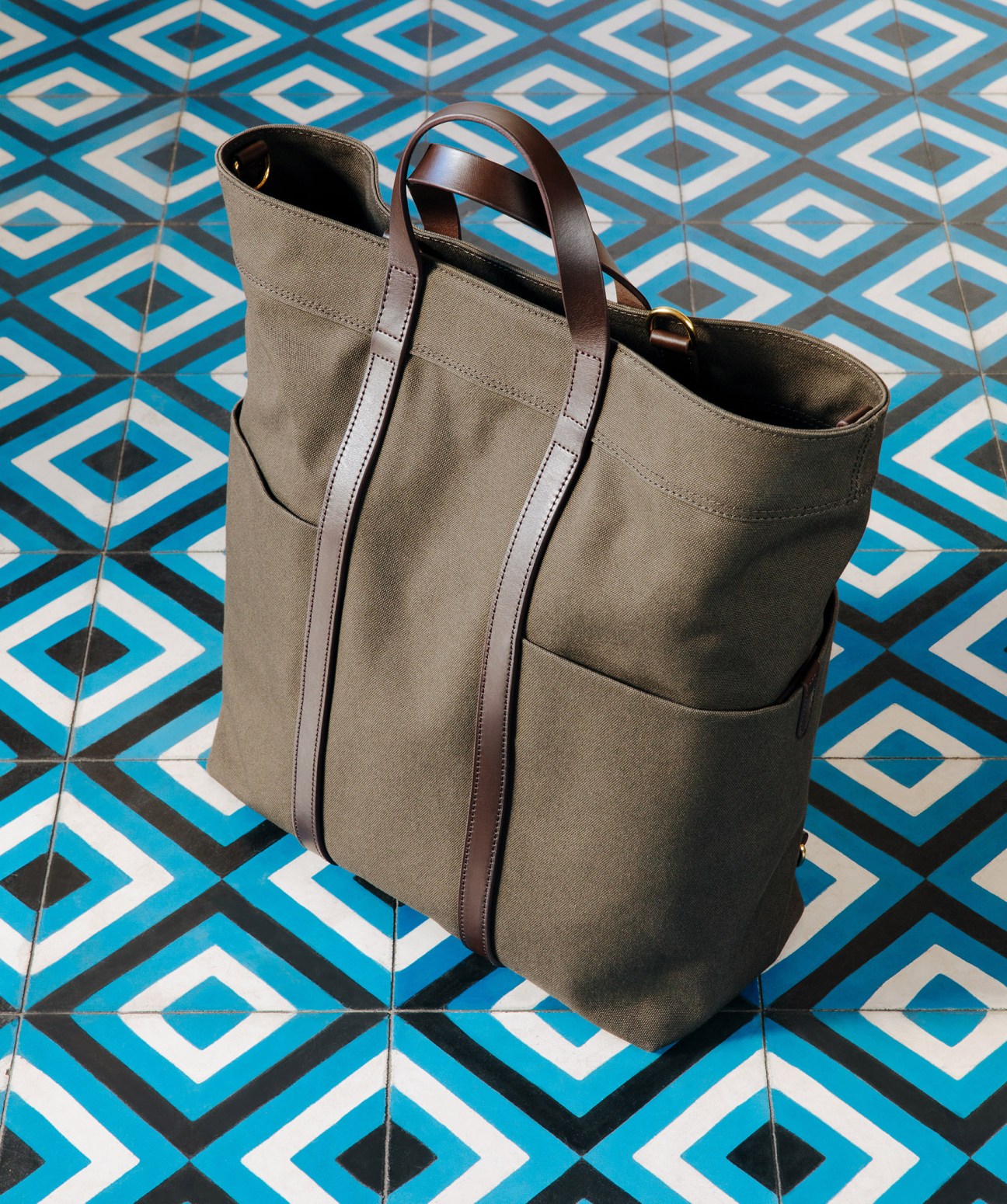 Canvas tote bag by Mismo with leather handles on geometric blue and white patterned tiles.