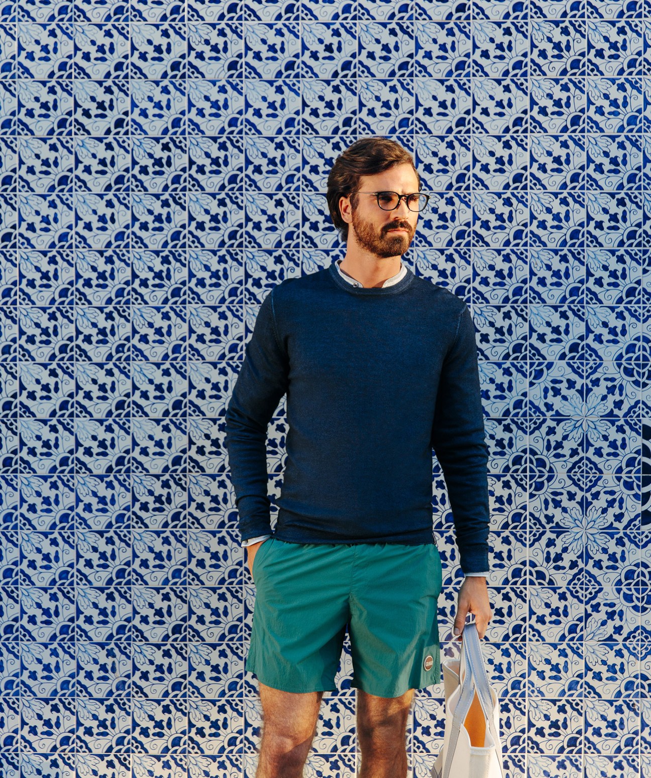 Man wearing navy jumper and teal shorts against blue and white patterned Portuguese tiles