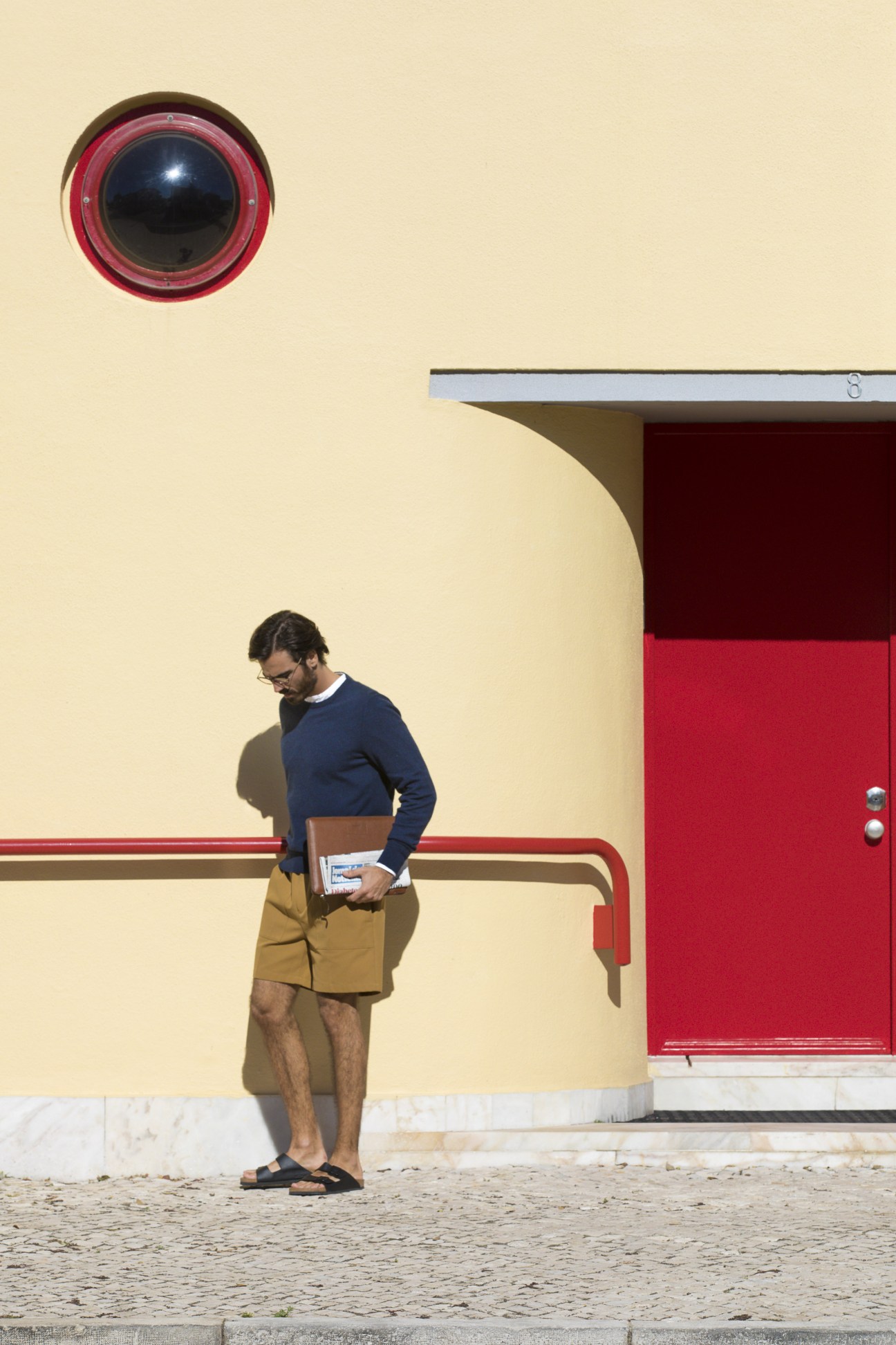 Man wearing Louis Vuitton jumper and Golden Goose shorts standing against yellow building with red door.