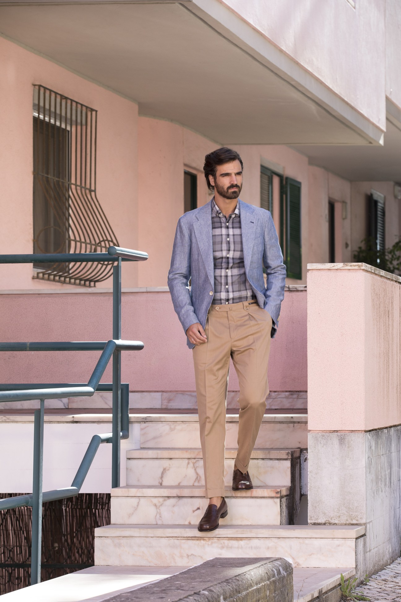 Man wearing blue jacket and checked shirt on steps in front of pink building in Lisbon