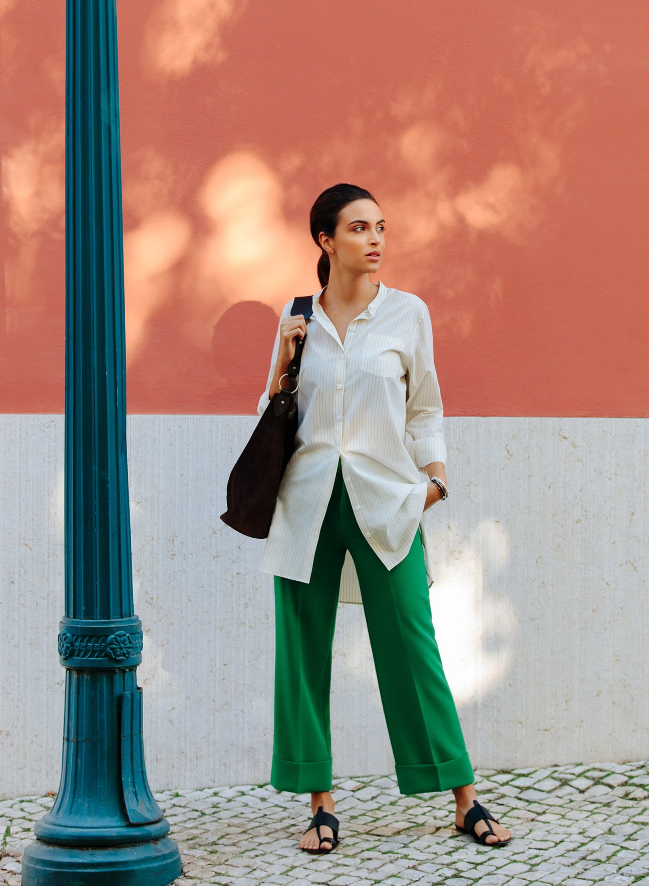 Woman in white shirt and green trousers standing against colorful Lisbon wall with blue column.