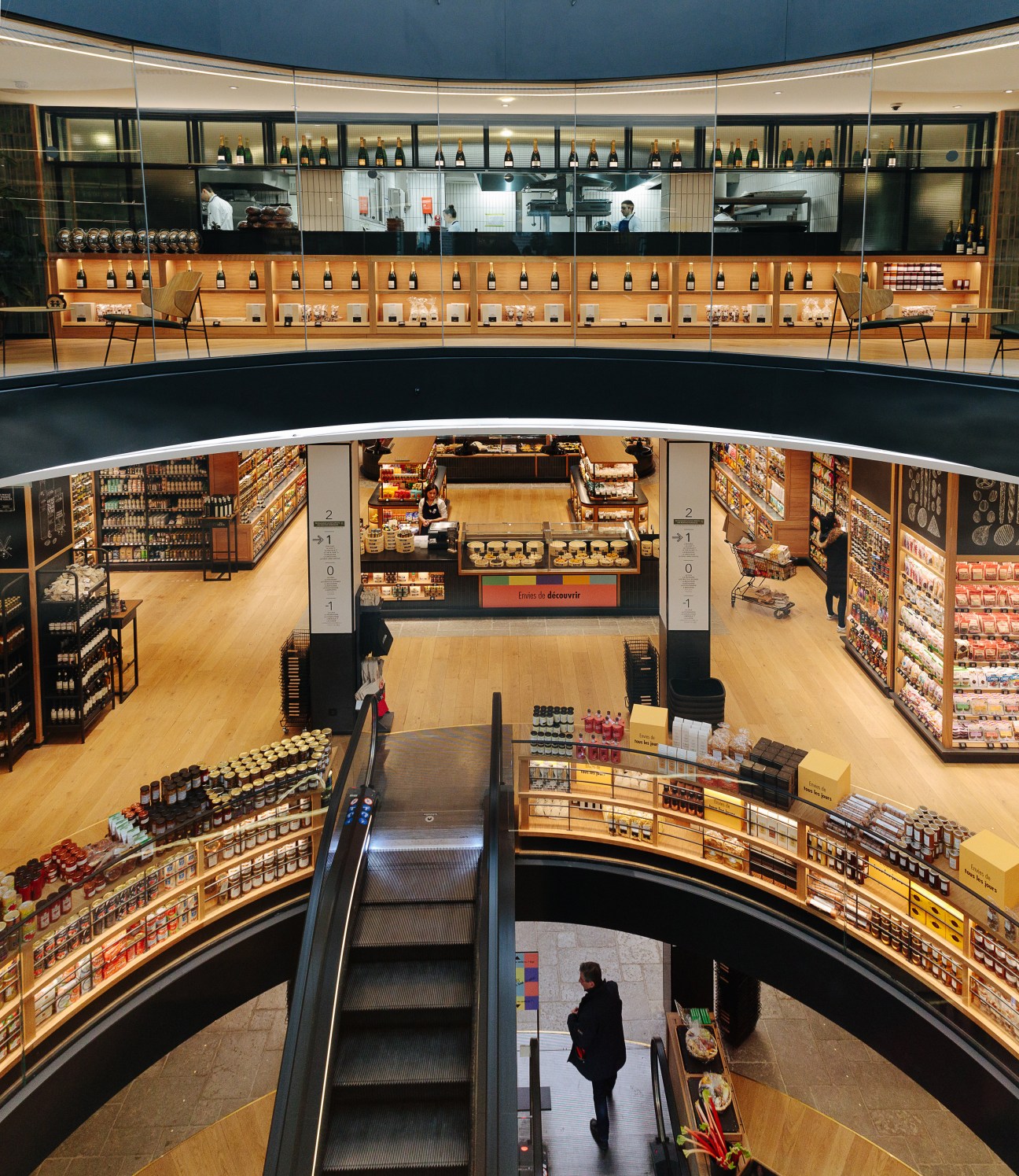 Aerial view of La Grande Épicerie's multi-level food hall with shelves of products, central checkout, and escalators.