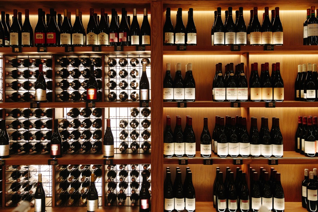 Wine bottles displayed on wooden shelves with warm lighting in La Grande Épicerie's wine cellar.
