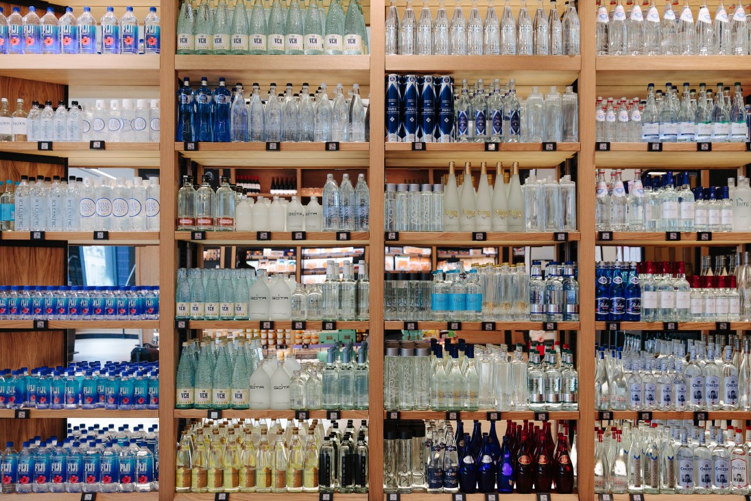 Wooden shelving unit displaying numerous bottles of mineral water from various international sources.