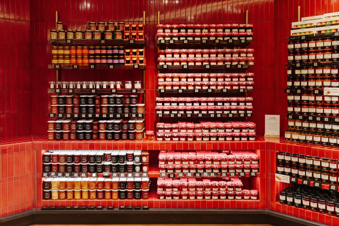 Shelves of jam jars displayed against red tiled wall at La Grande Épicerie Passy.