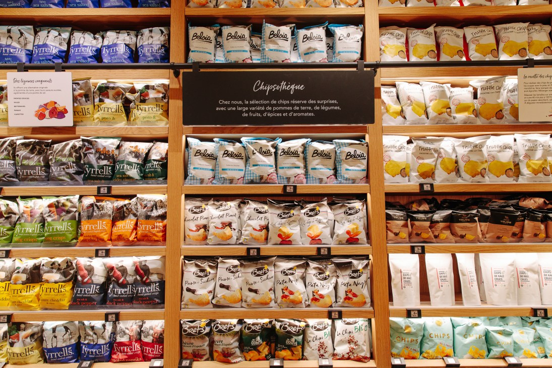 Wooden shelving displaying Grande Épicerie's chipsothèque with 100 varieties of crisps in organized rows.