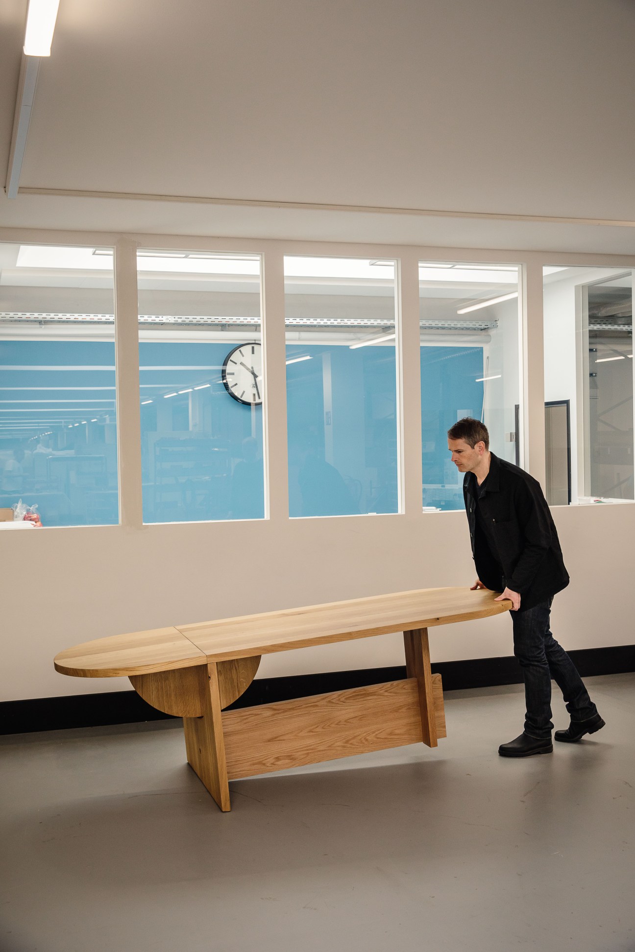 Wolfgang Hartauer stands beside his wooden Lot table in a modern office with blue-tinted windows.
