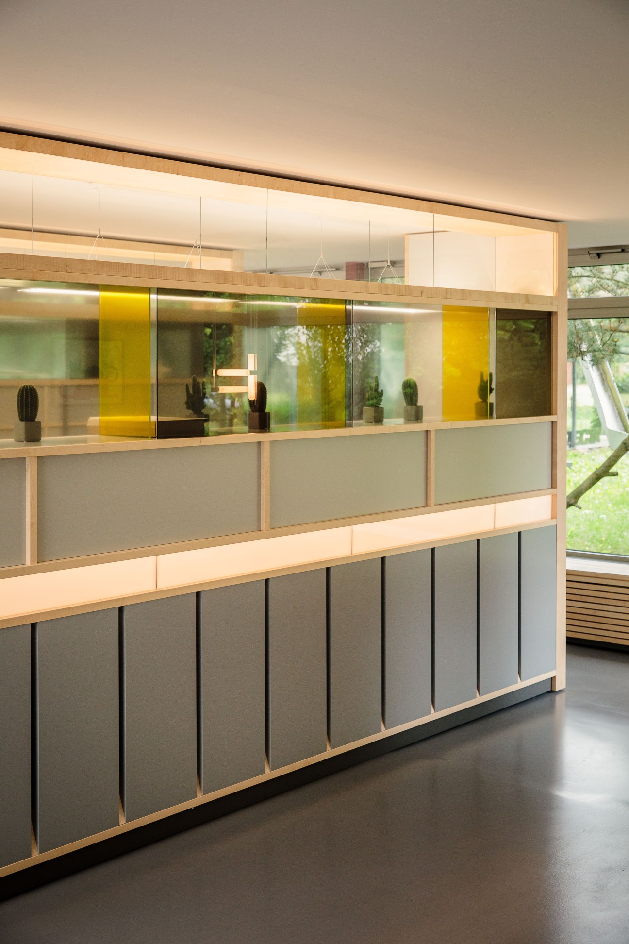 Modern office interior with wooden and glass display shelving featuring yellow accents and views of green landscape.