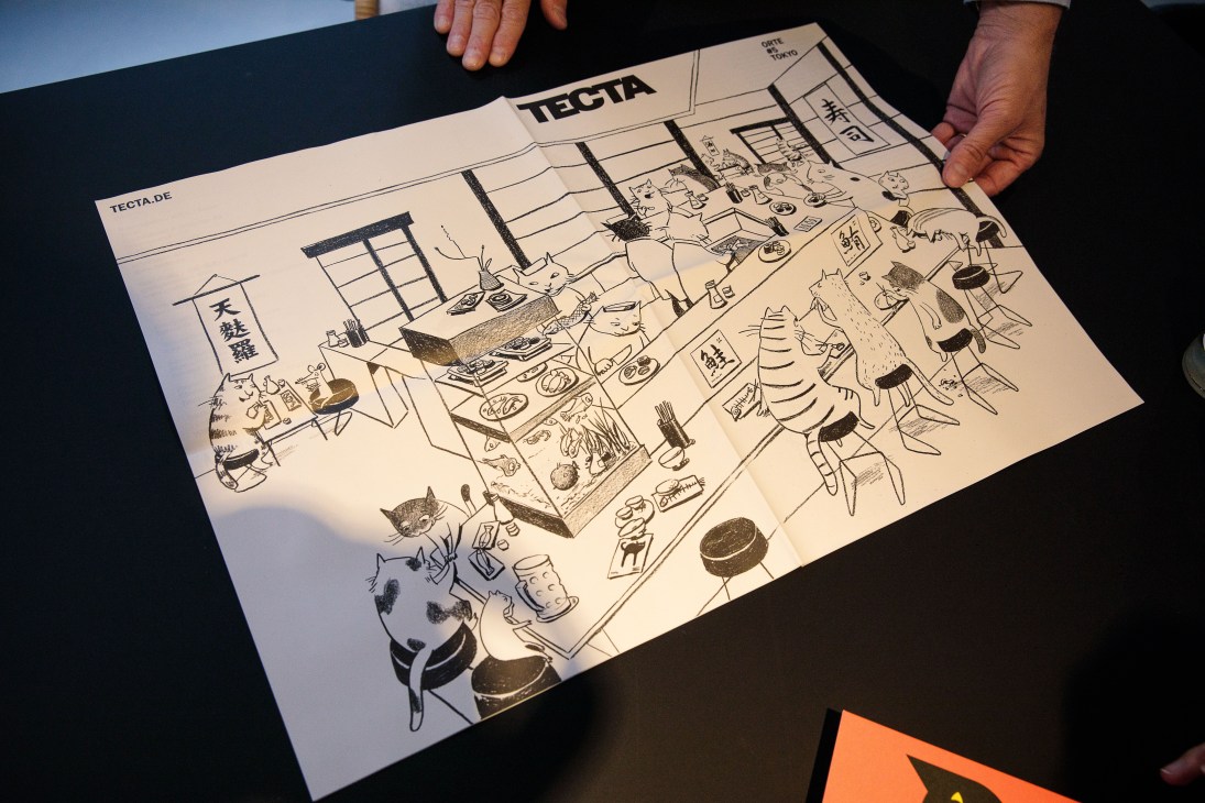 Hands holding an illustrated Tecta catalogue for Japan featuring line drawings and Japanese text.