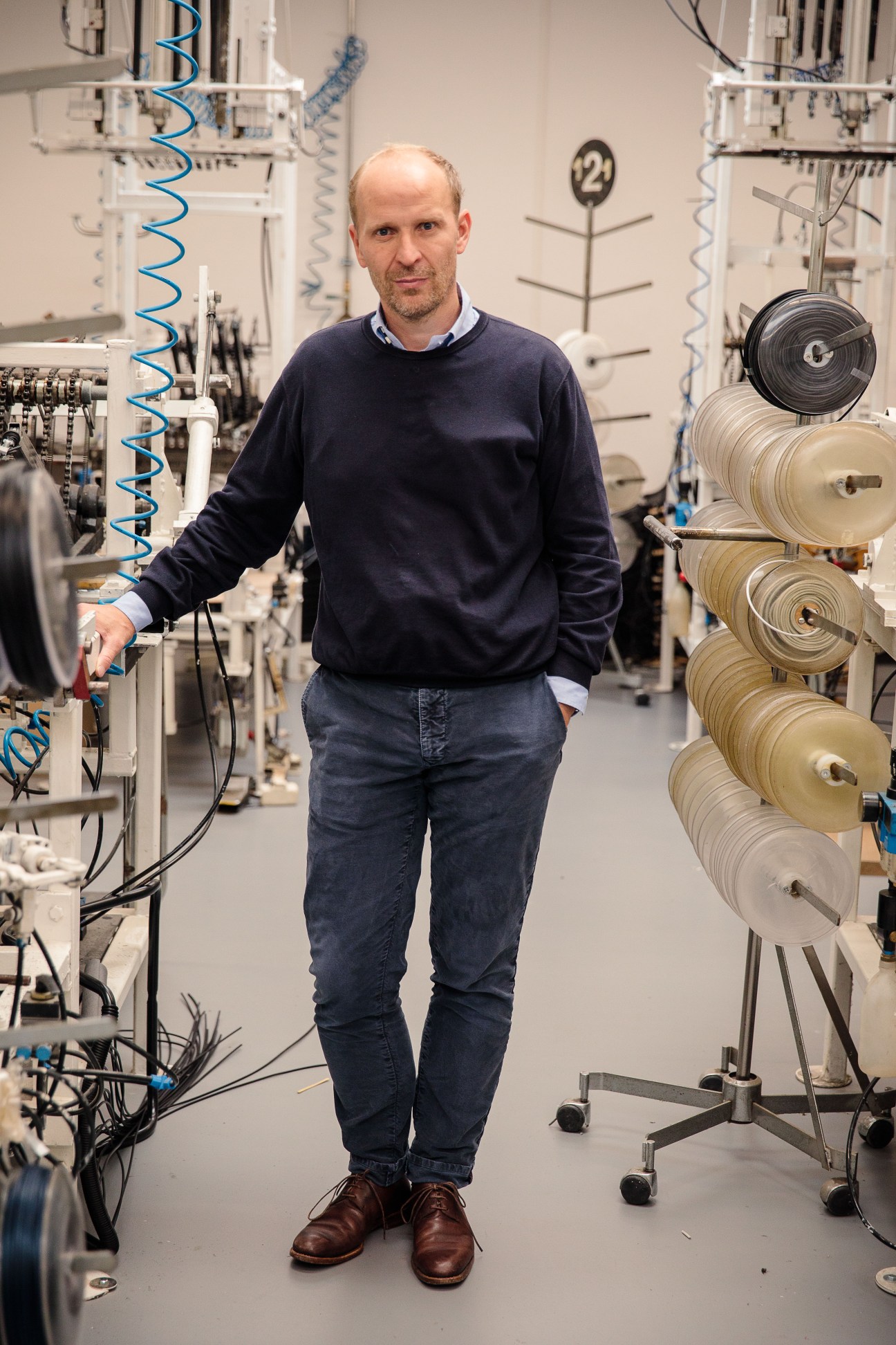 Christian Drescher stands in Tecta's factory surrounded by spools of fabric and weaving equipment.