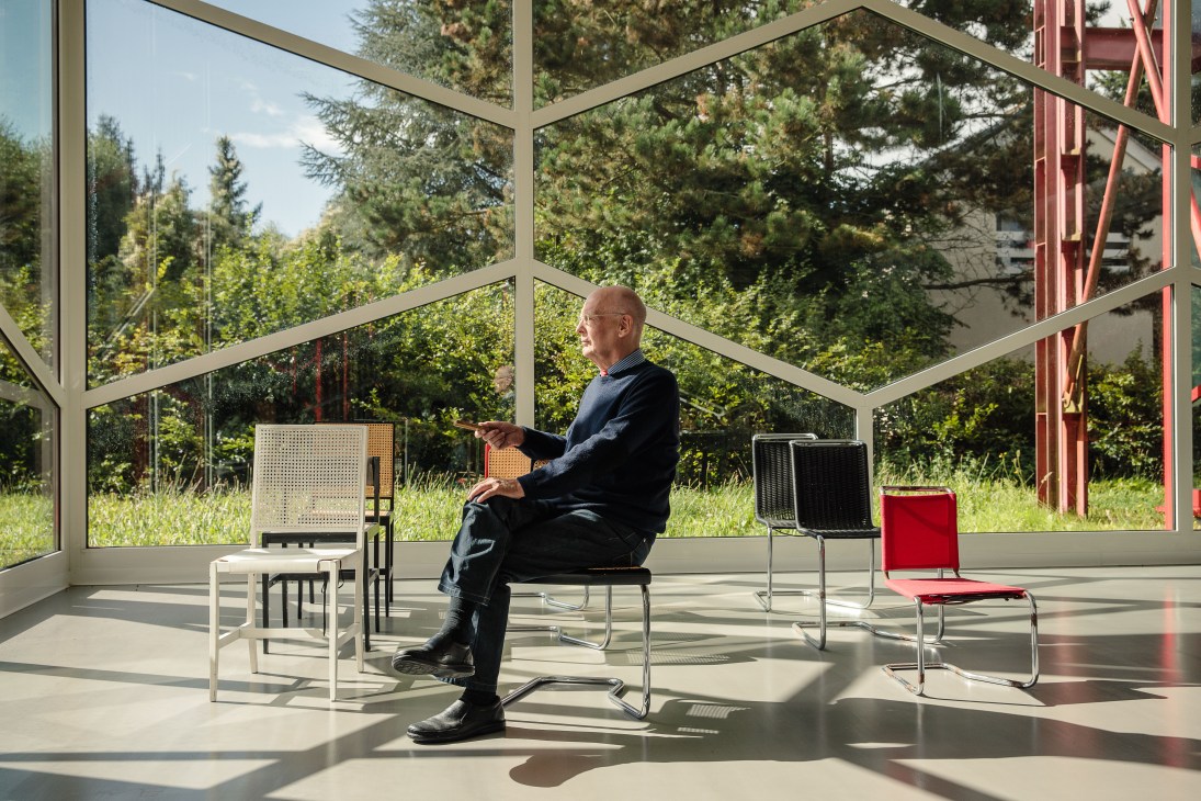 Axel Bruchhäuser sits in a modernist office with large geometric windows overlooking green forest, surrounded by Bauhaus furniture designs.