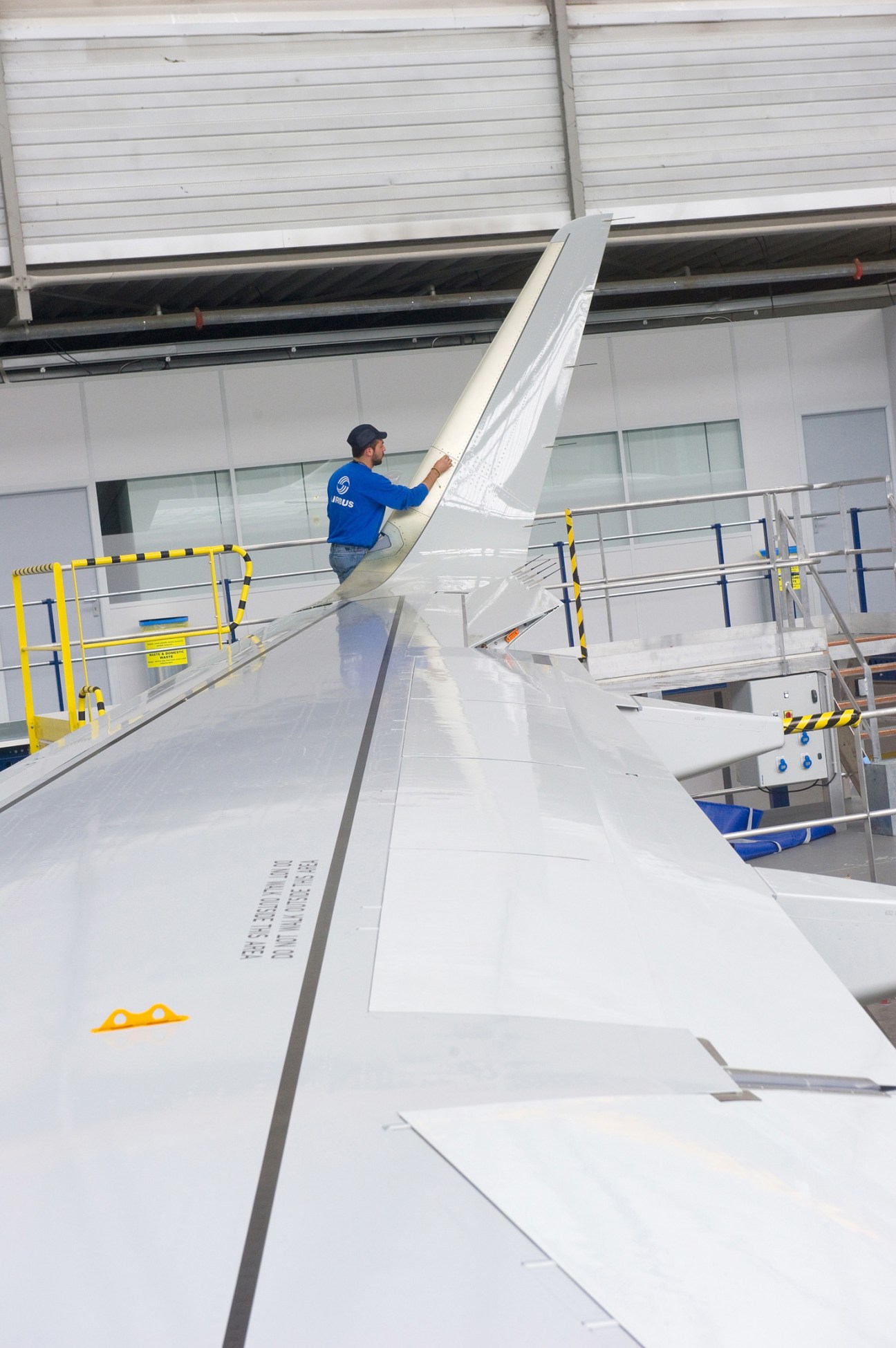 Worker in blue jacket installing A320 Sharklet winglet on aircraft fuselage during assembly