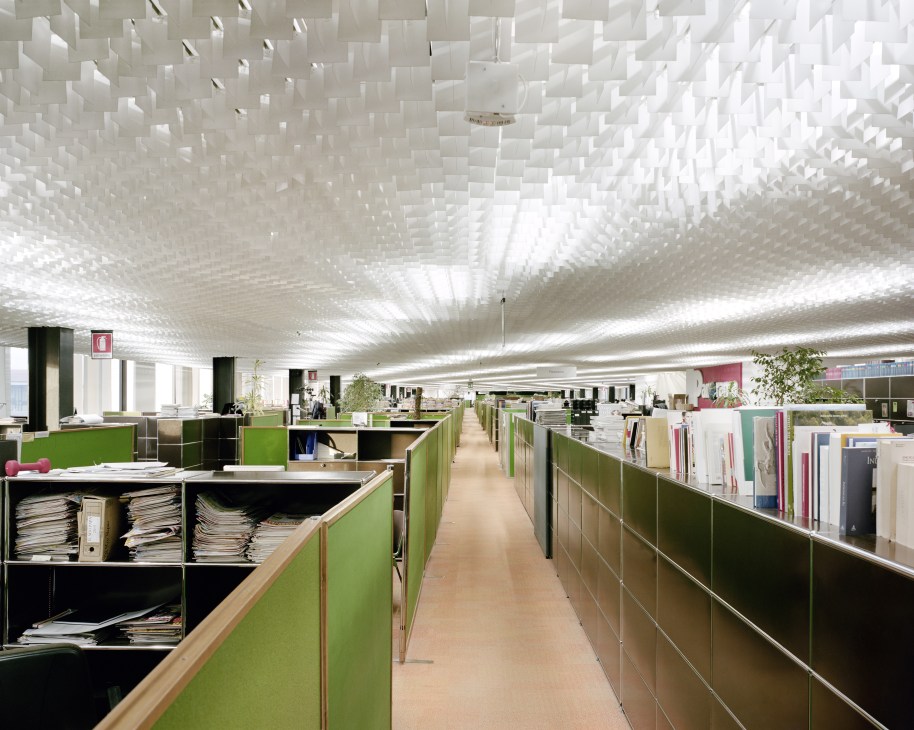 Open-plan office space with green partition walls and geometric white ceiling design at Palazzo Mondadori.