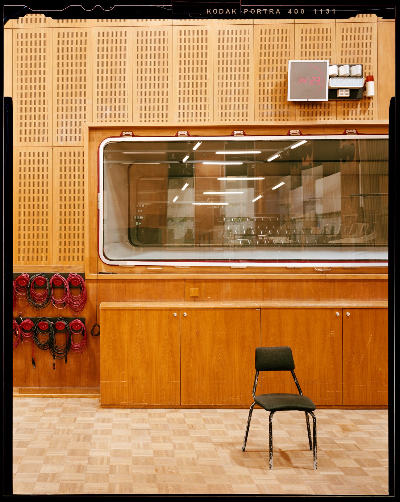 Recording studio with wood paneled walls, glass window, control equipment, and single chair