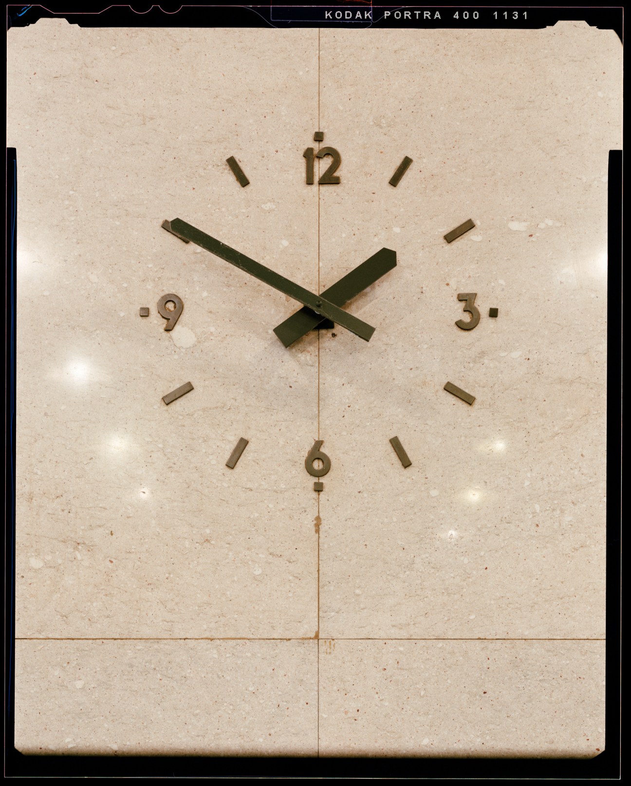 A vintage clock face with green hands showing approximately 10:10, photographed on film with visible grain and aging