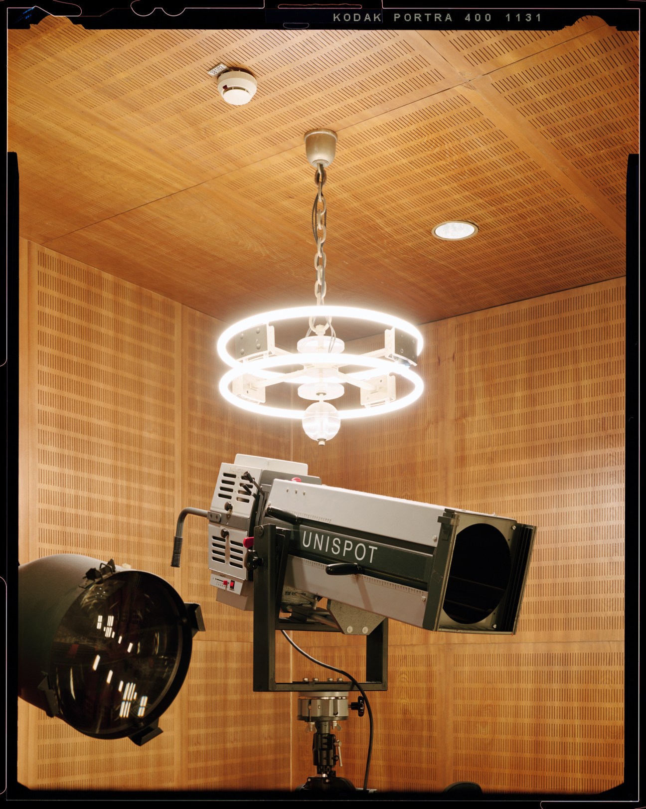 Recording equipment including UNISPOT device on tripod with chandelier and wood-paneled walls in broadcast studio