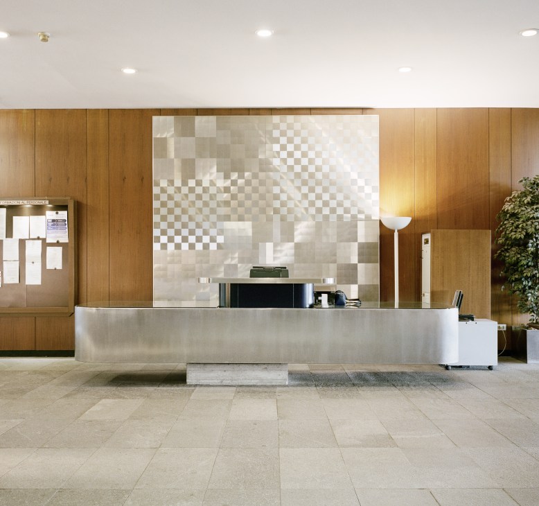 Modern reception desk with metal counter and patterned tile backdrop in wood-paneled lobby