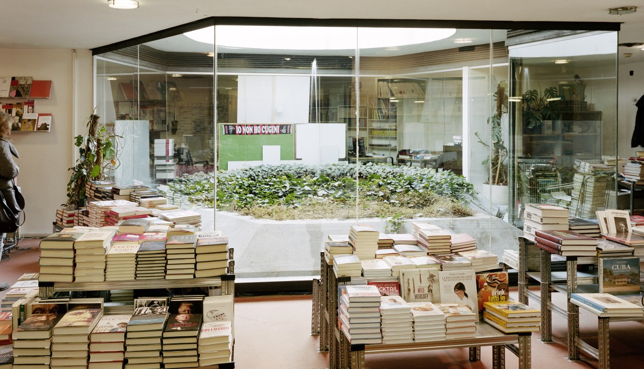 Interior of Mondadori's in-house bookshop with stacked books on wooden shelving and glass storefront.