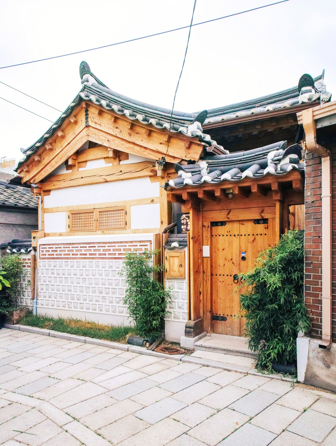 Traditional Korean hanok with wooden exterior, decorative tiled roof with upturned eaves, and wooden entrance door in Seochon.