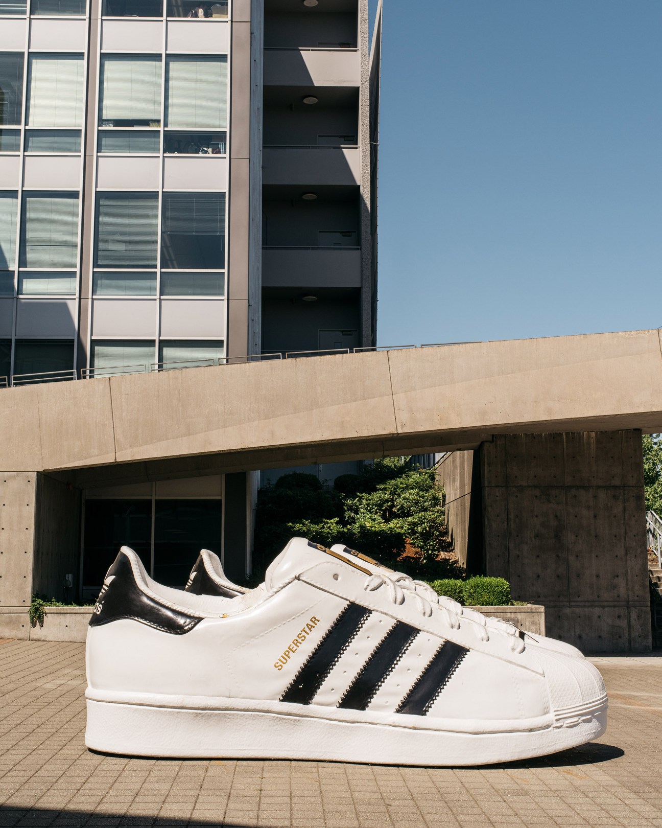 Giant oversized Adidas Superstar trainer with white leather and black stripes displayed outdoors.