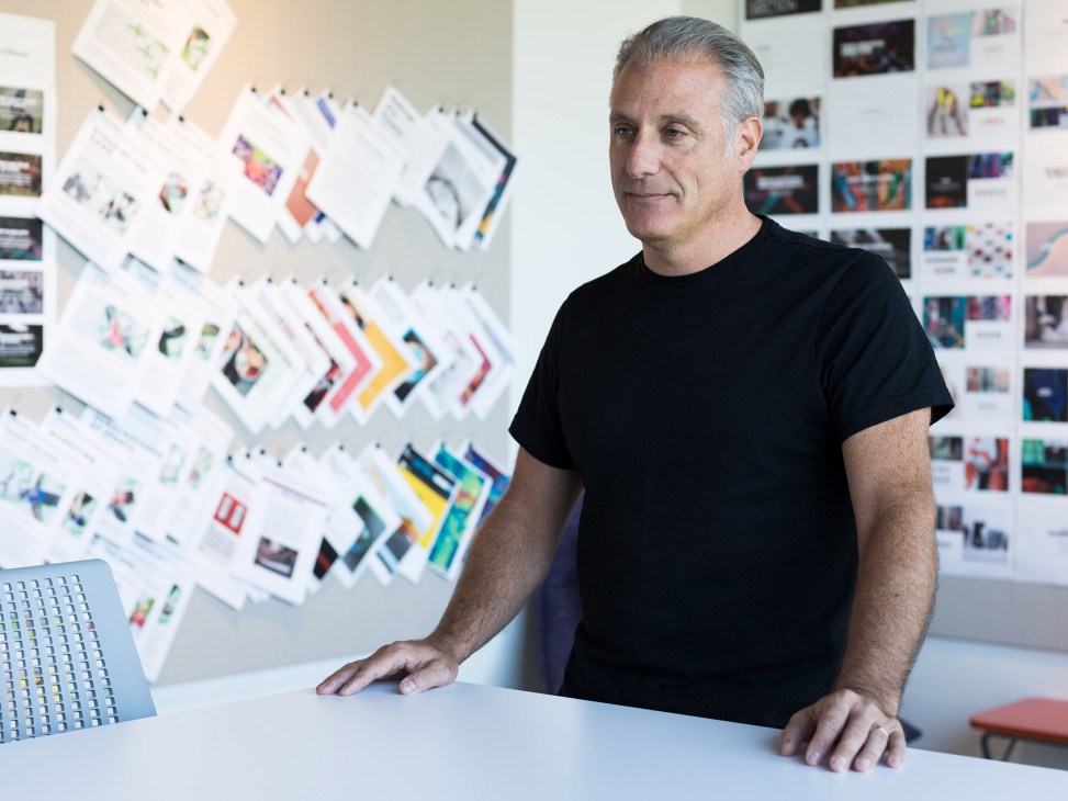 Paul Gaudio, Adidas global creative director, stands at a white table in a modern office with design boards on the wall behind him.