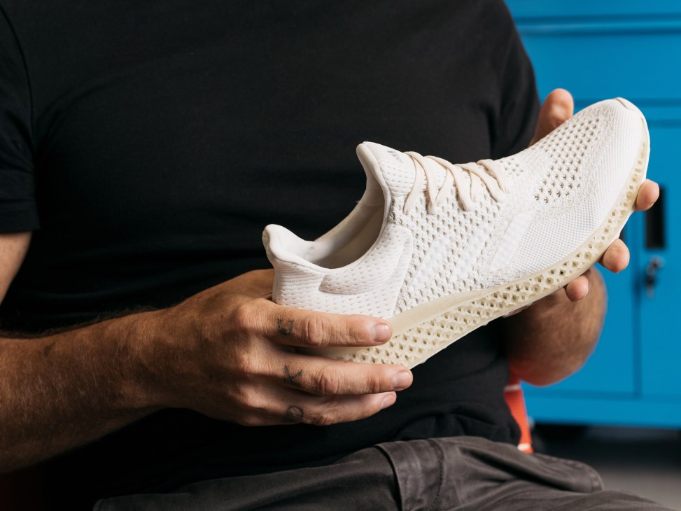 Hands holding a white Adidas Futurecraft 3D-printed shoe against a blue background