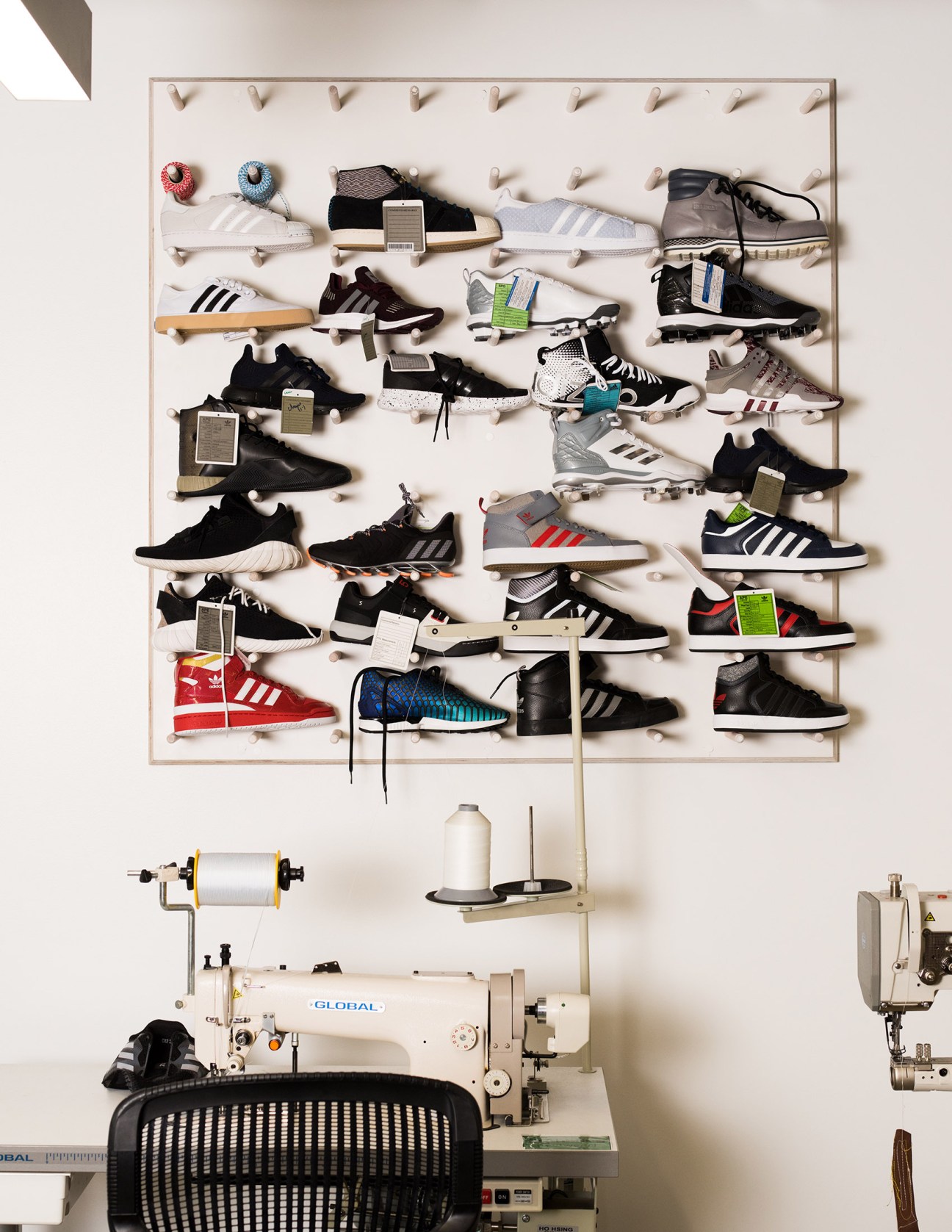 Wall display of various Adidas prototype sneakers mounted on pegs above sewing equipment in a design studio.