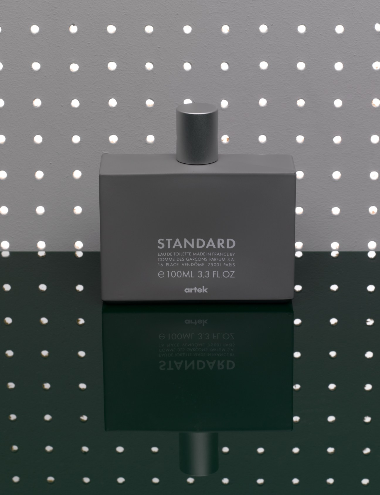 Artek Standard fragrance bottle by Comme des Garçons against a dotted background.