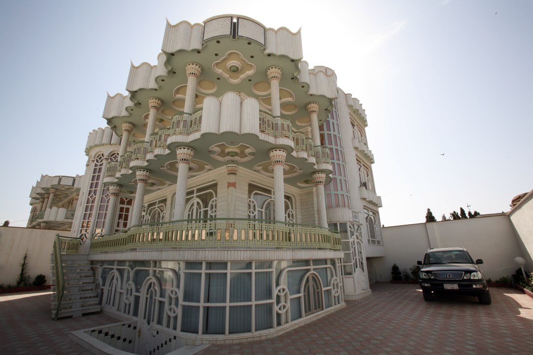 Ornate multi-story mansion with elaborate columns, decorative elements and mirrored glass exterior in Herat, Afghanistan with a dark SUV parked in driveway.