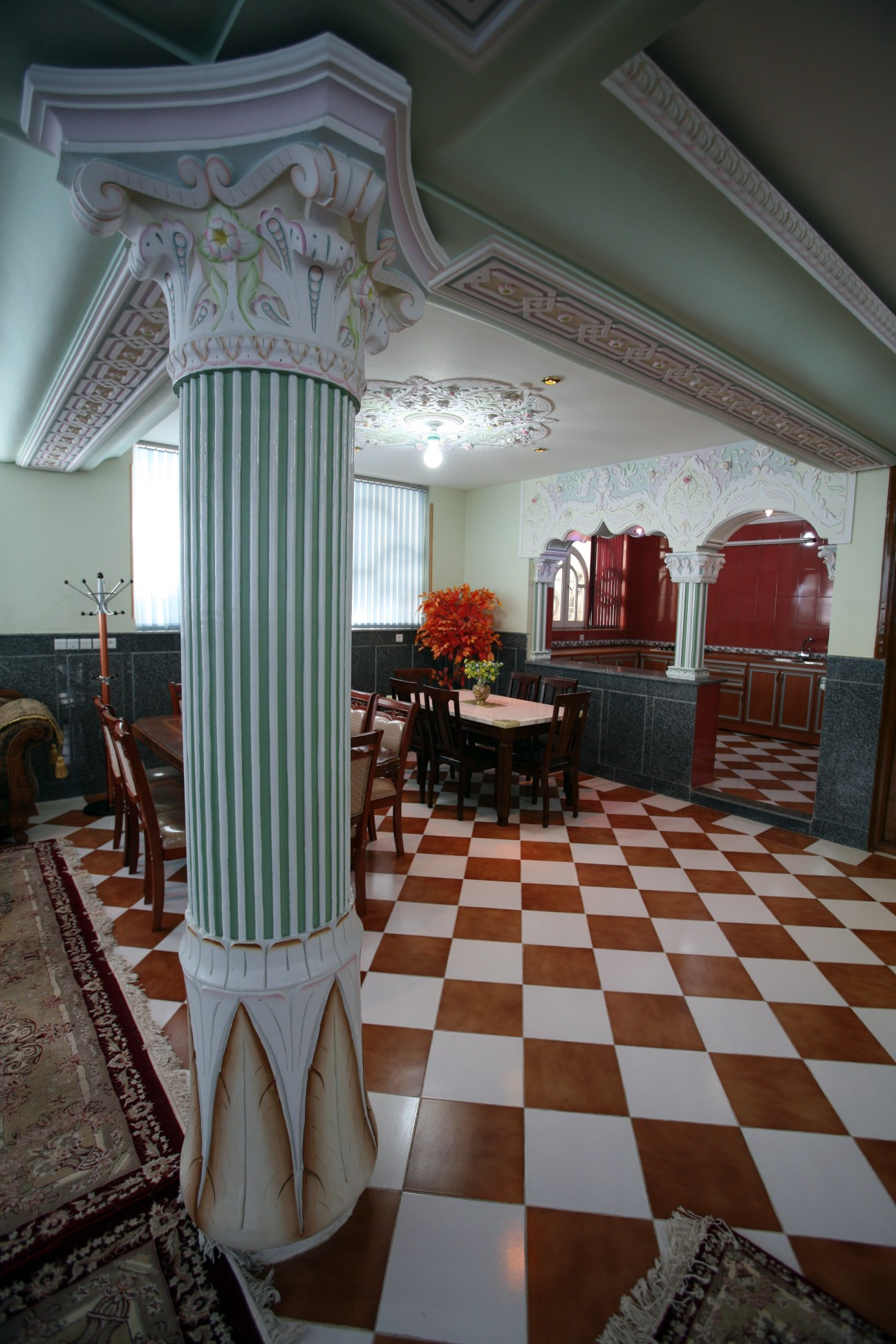 Interior of a basement with ornate white columns, checkered floor, and decorative elements including plastic flowers and red furniture.